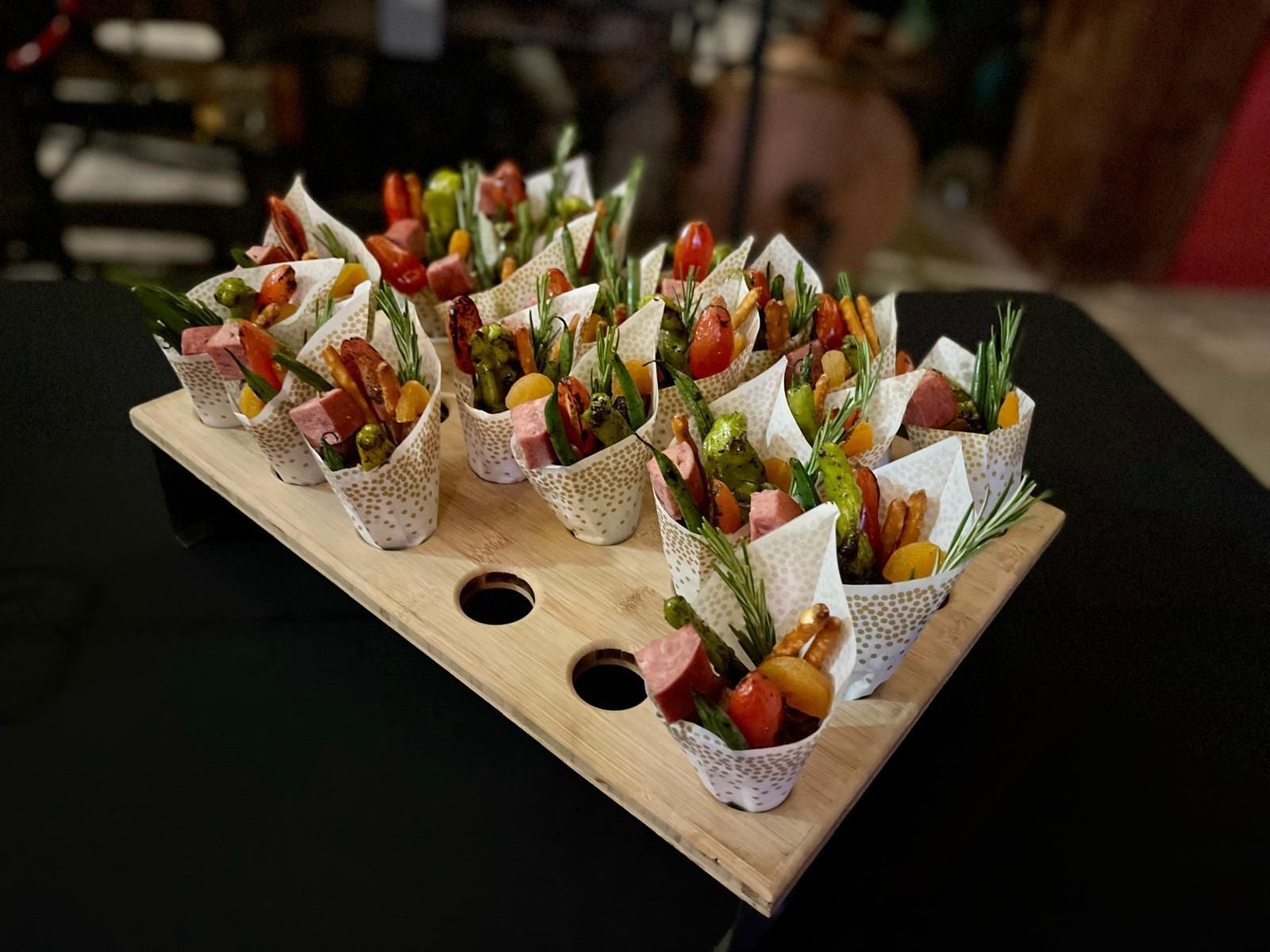Tray of appetizer cones with vegetables, tomatoes, and meat, on a wooden board.