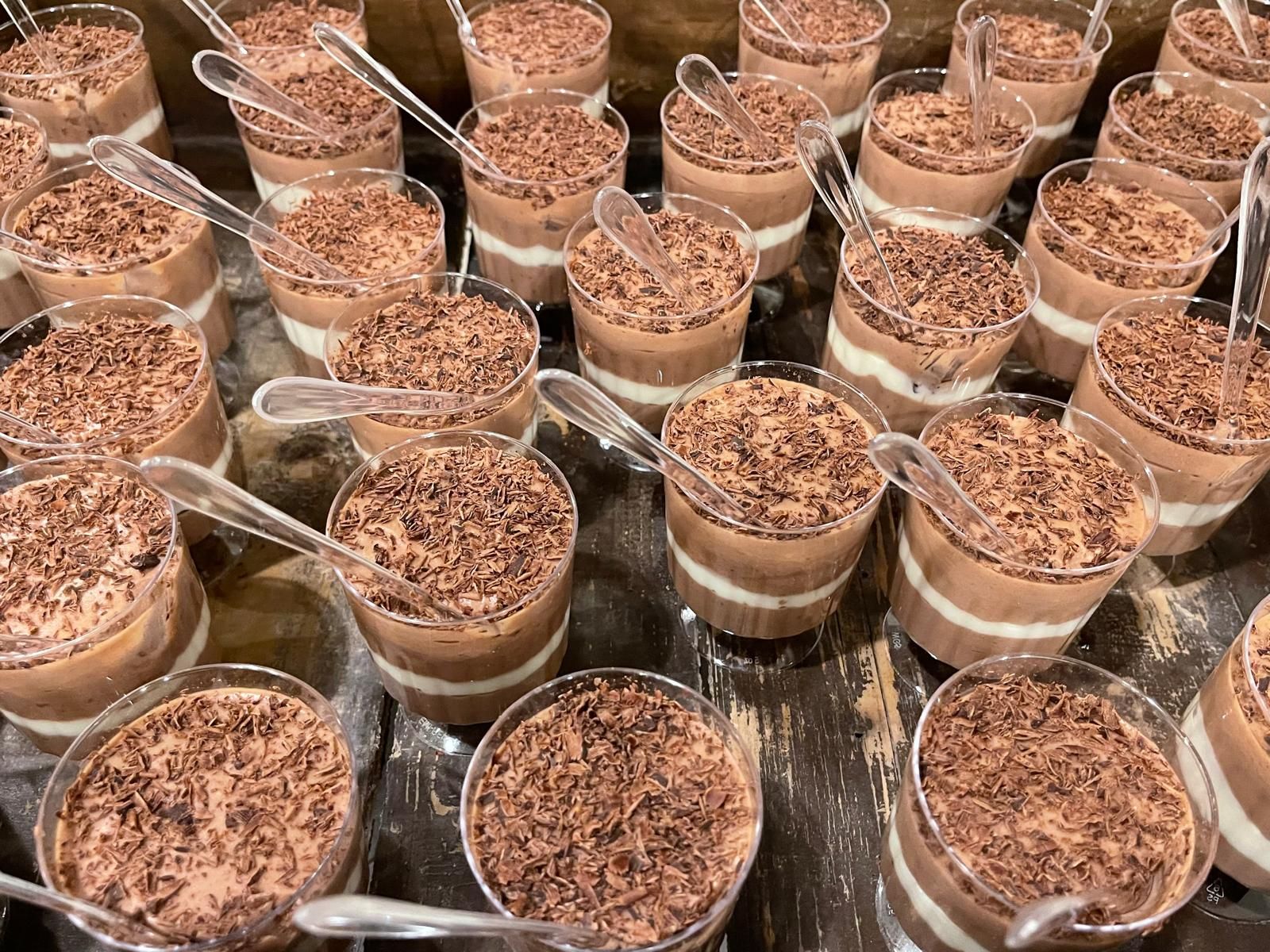 Rows of chocolate parfaits in clear cups, topped with chocolate shavings, each with a small spoon.