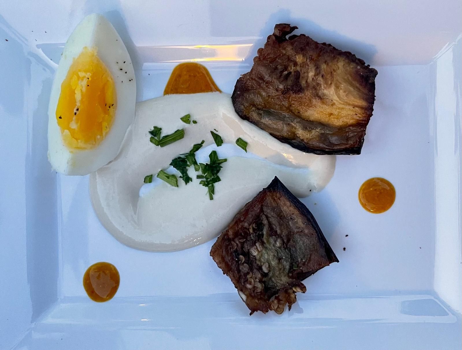 Plate with seared fish, soft egg, creamy sauce, and dots of orange sauce.