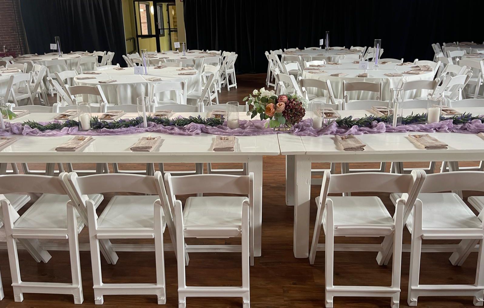 White tables and chairs set up for an event, decorated with floral centerpieces.