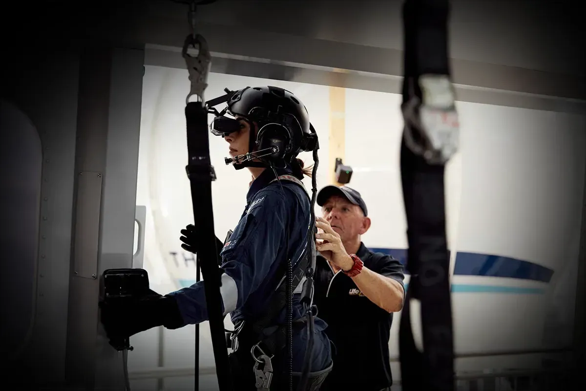 Instructor checking a rear crew member's harness at the door of the AW-139 rear crew trainer