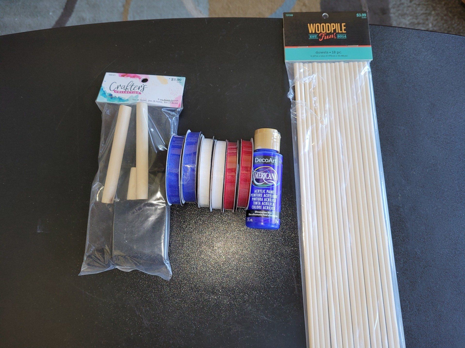 A bottle of acrylic paint sits on a table next to wooden sticks