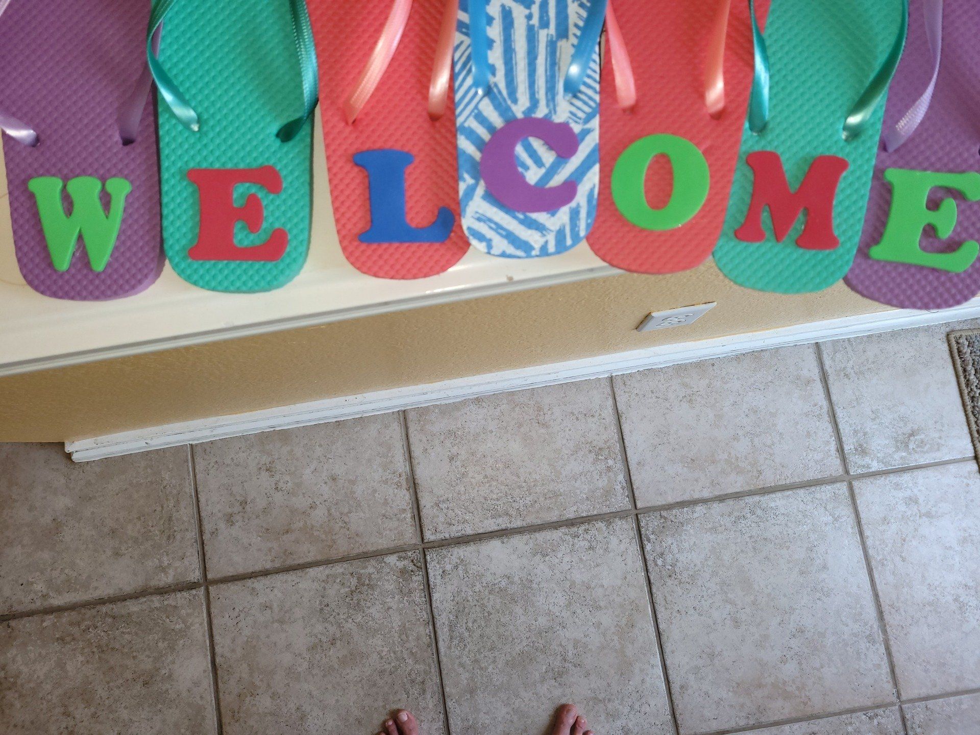 A welcome sign made out of flip flops on a tiled floor