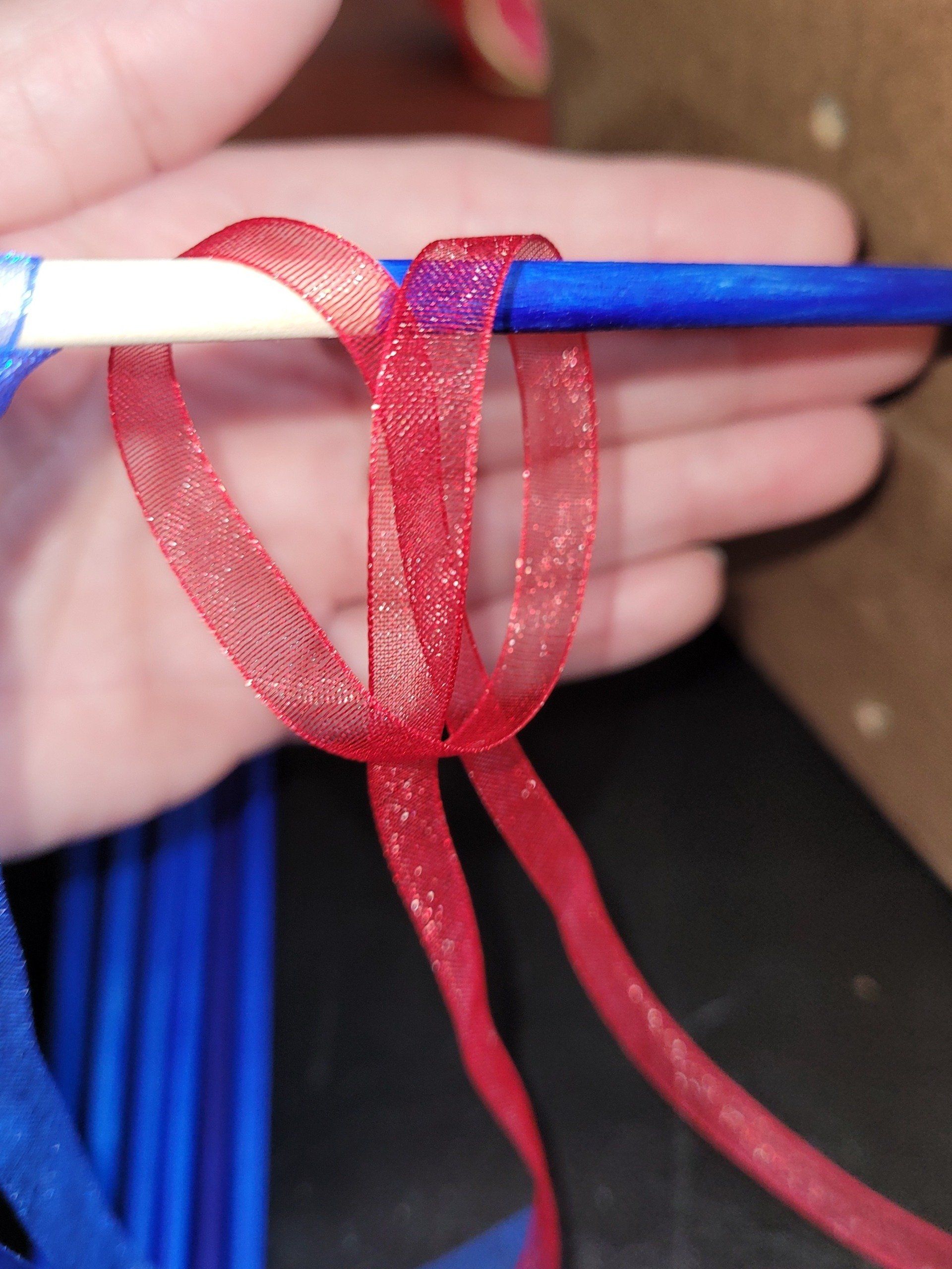 A person is holding a blue pencil with a red ribbon tied around it