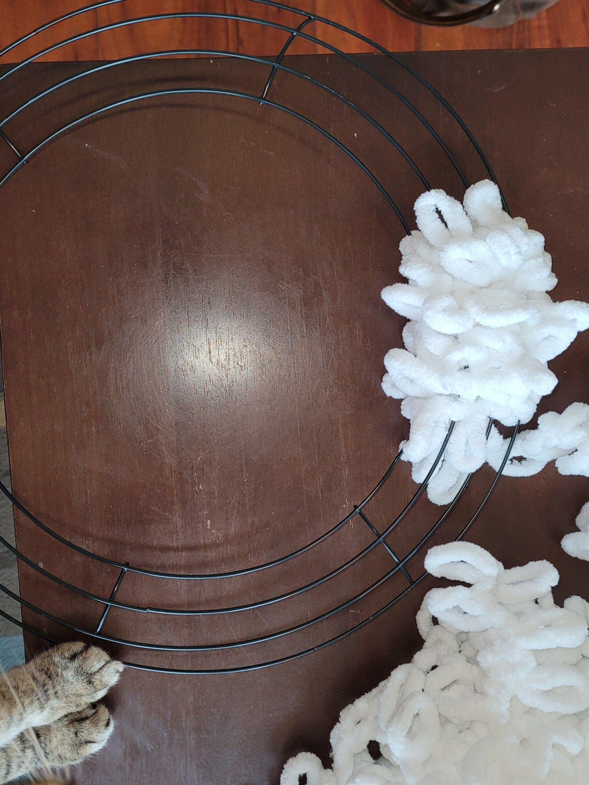 A cat standing next to a wire wreath on a table