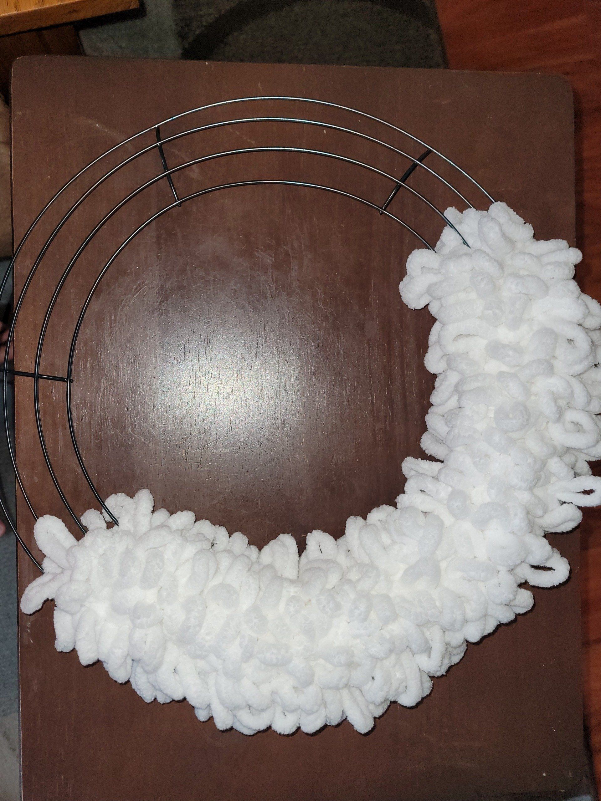 A wreath made of white yarn is sitting on a wooden table