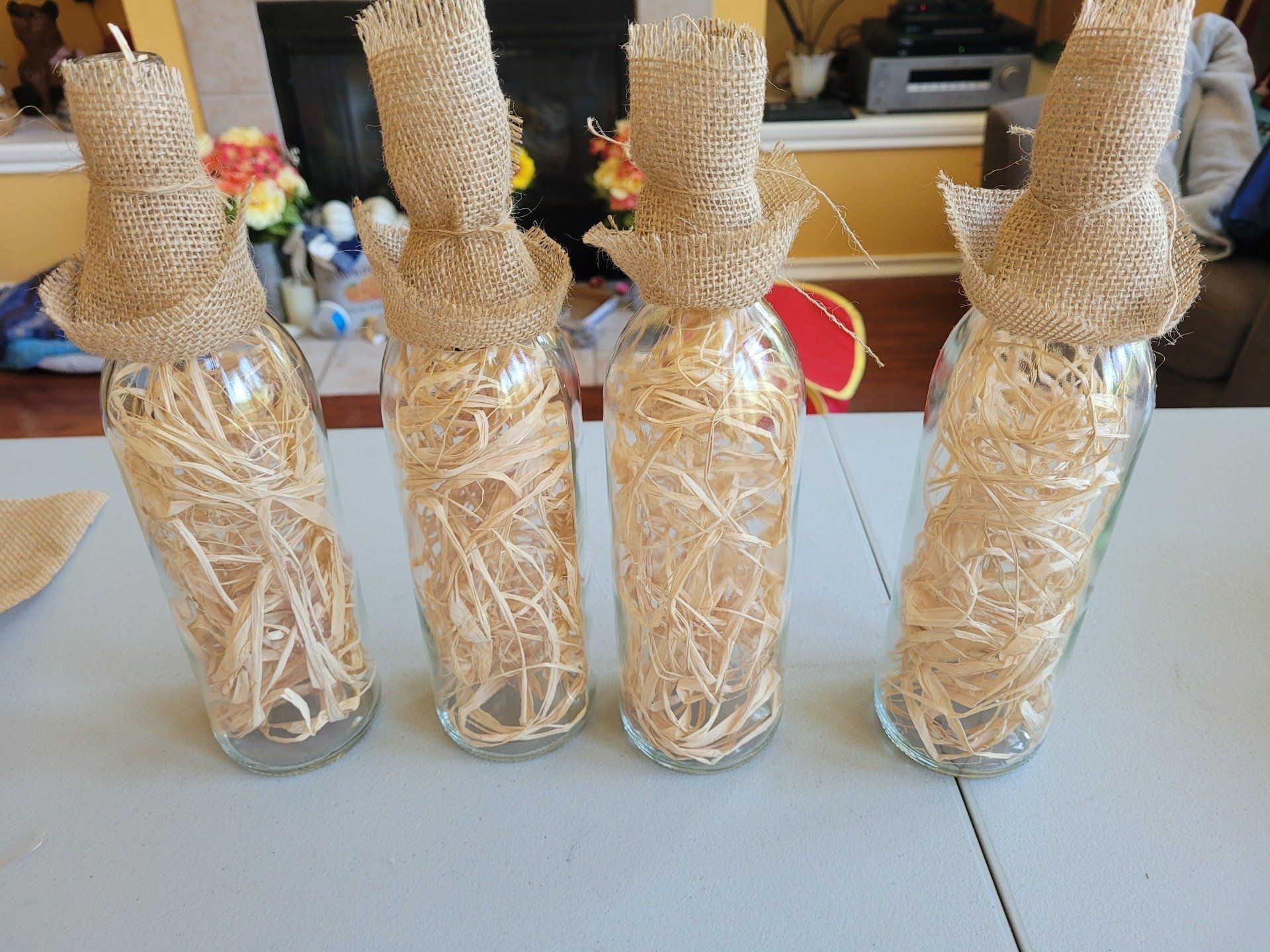 Four bottles filled with hay are sitting on a table
