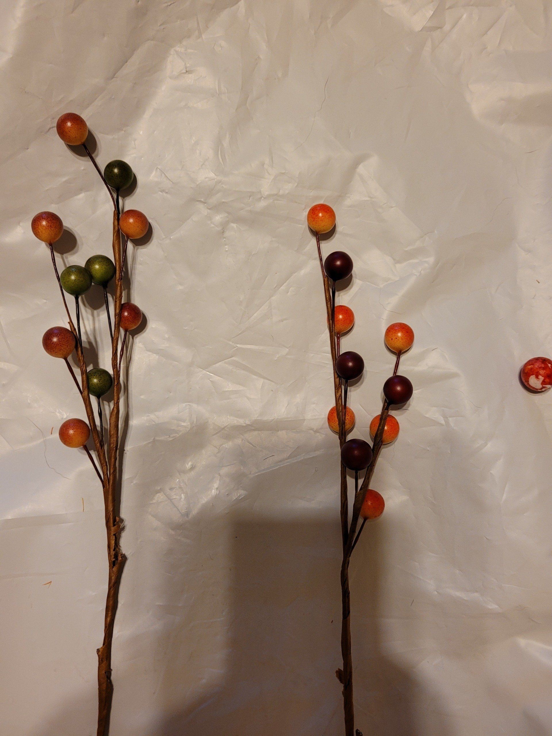Three branches with berries on them on a white surface