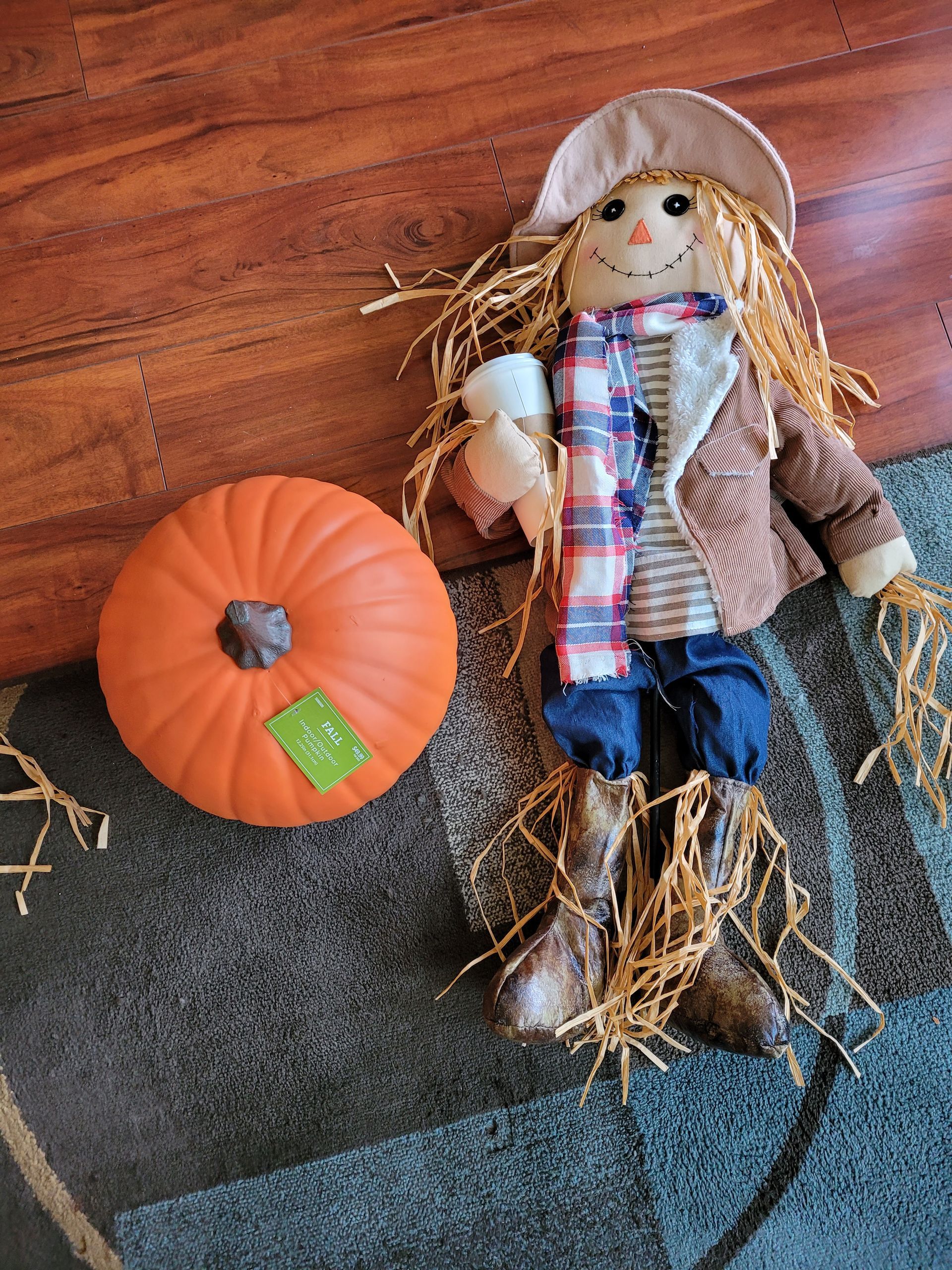 A scarecrow is sitting on a rug next to a pumpkin.