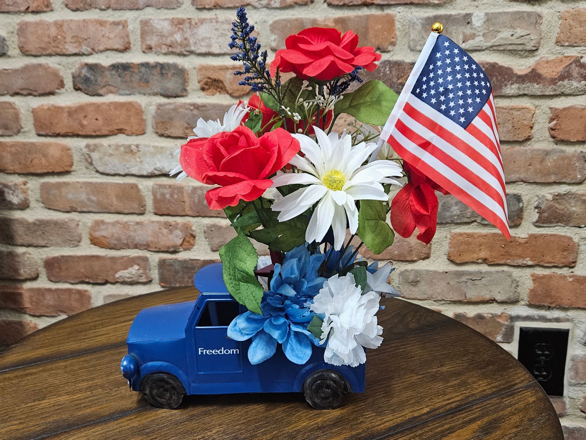 A blue truck filled with red , white and blue flowers and an american flag.