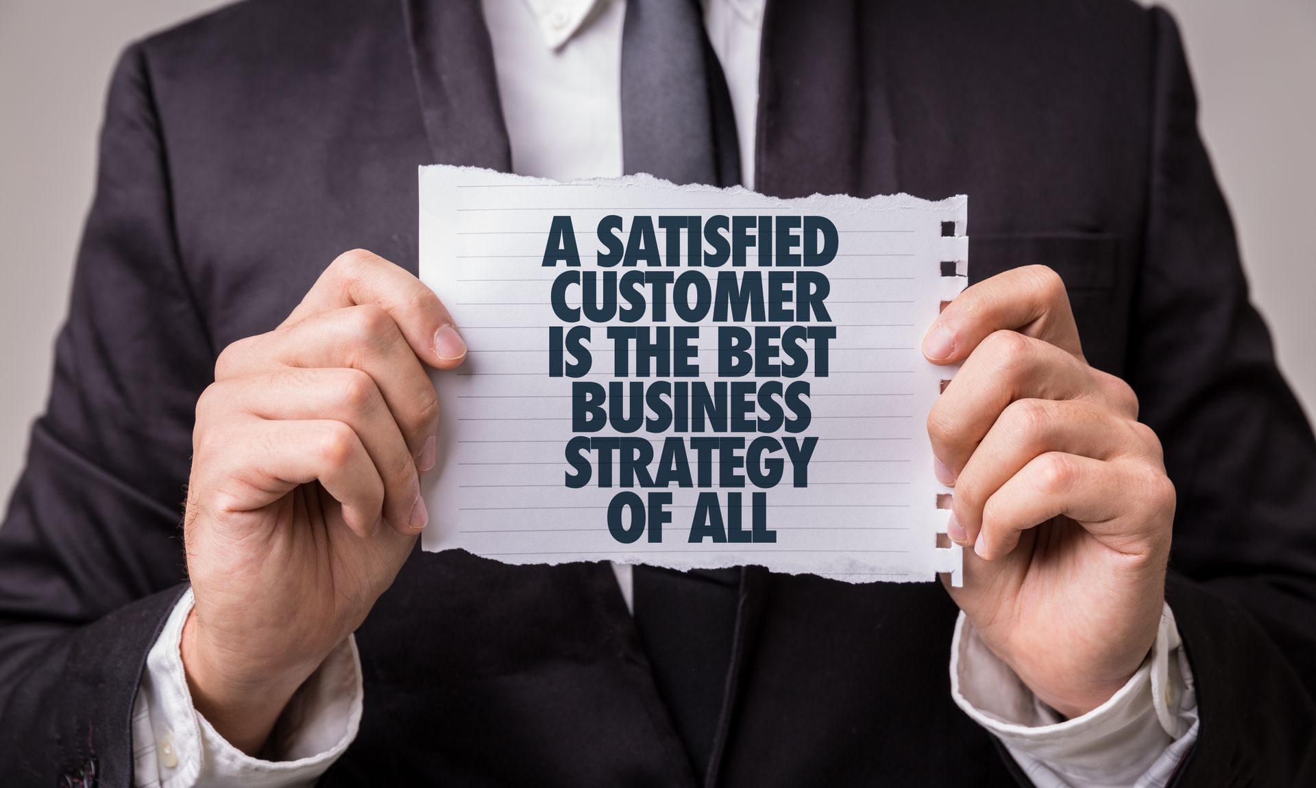 A man in a suit is holding a piece of paper that says a satisfied customer is the best business strategy of all.