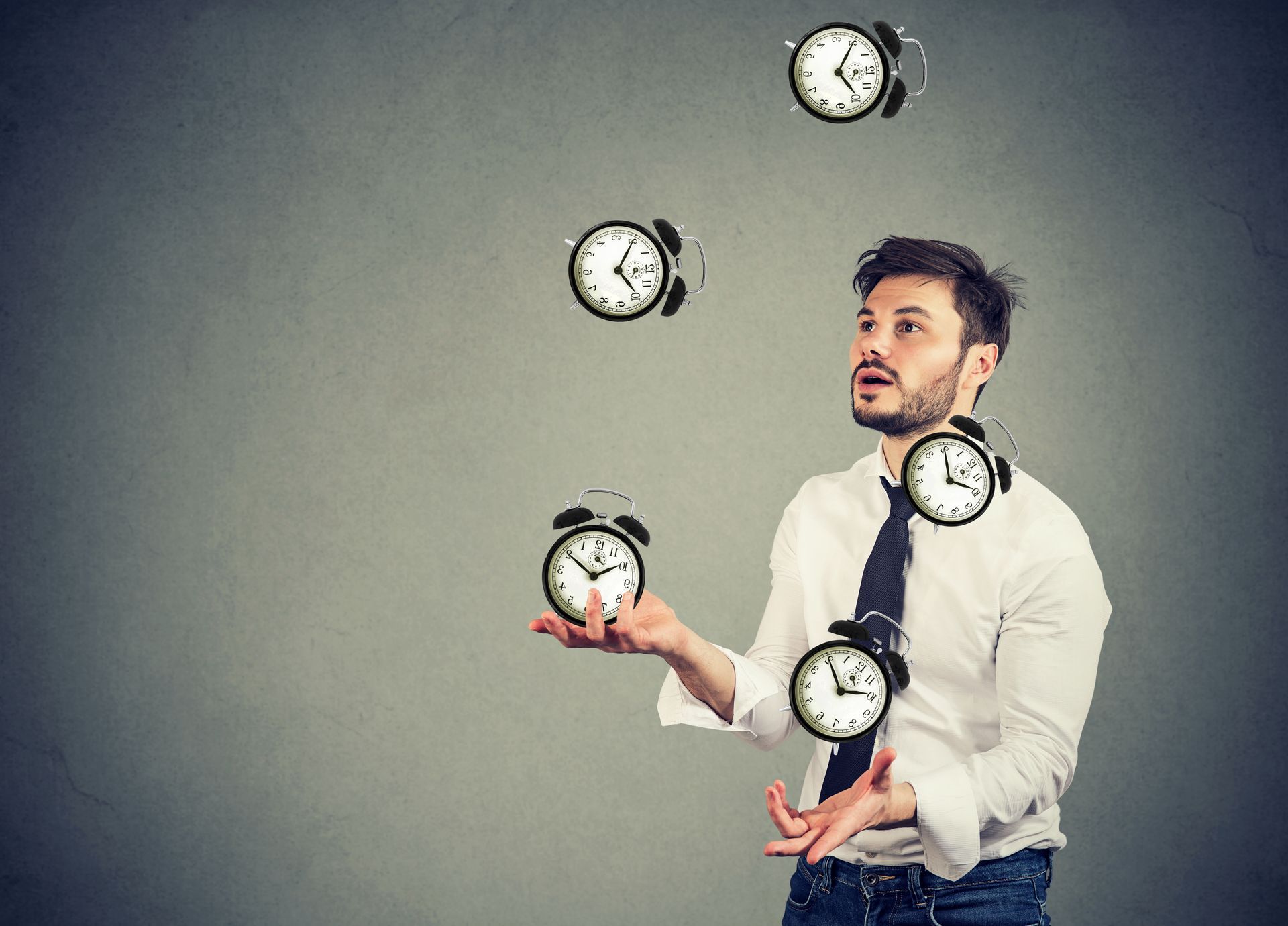 A man is juggling three alarm clocks in his hand.