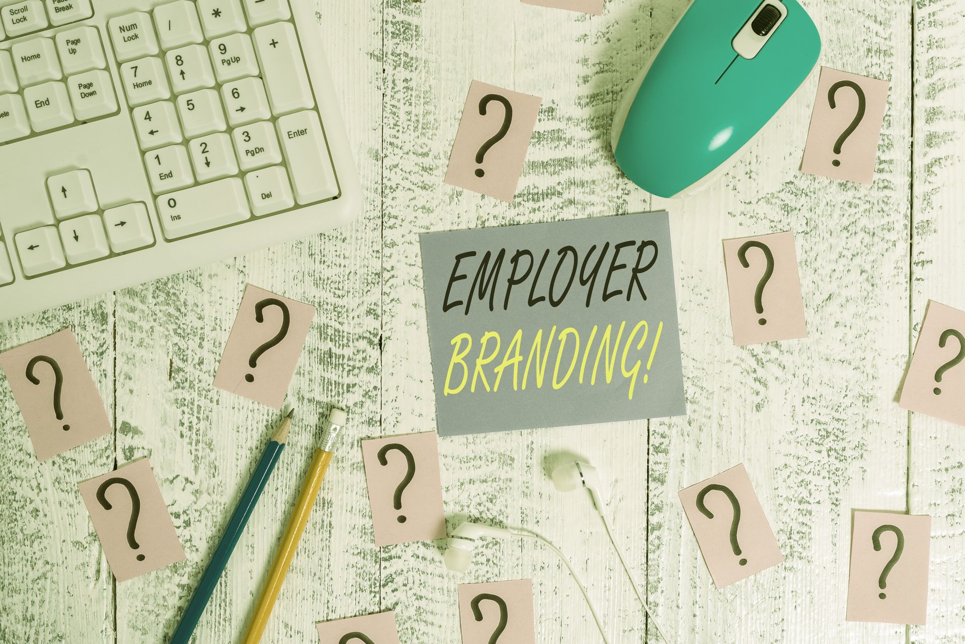 A wooden table with a keyboard , mouse , pencils and a note that says employer branding.