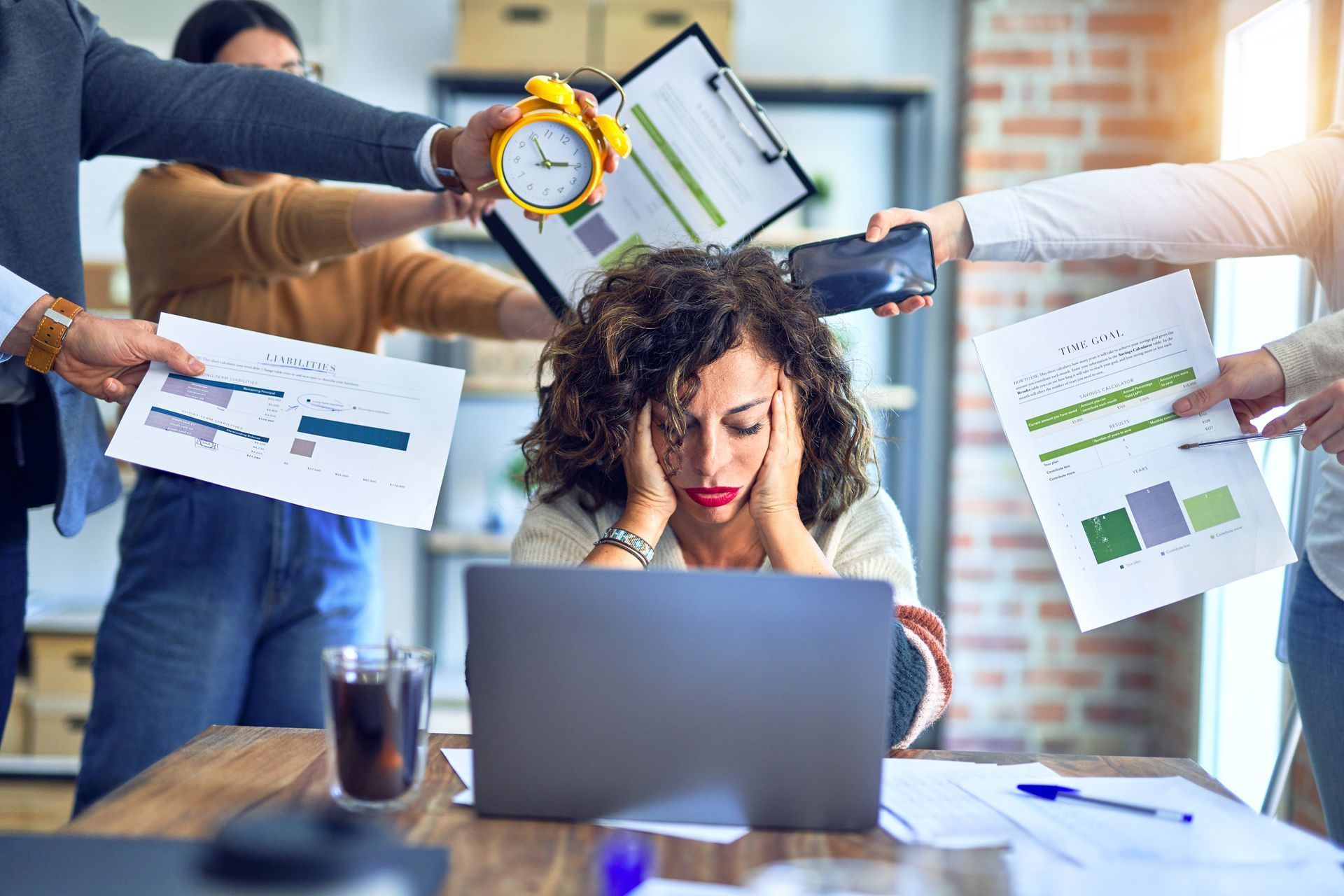 A woman is sitting in front of a laptop computer surrounded by people holding papers.
