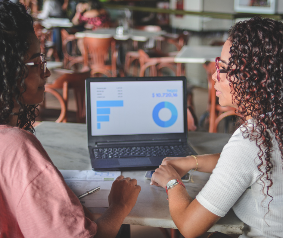 Two women are sitting at a table looking at a laptop.