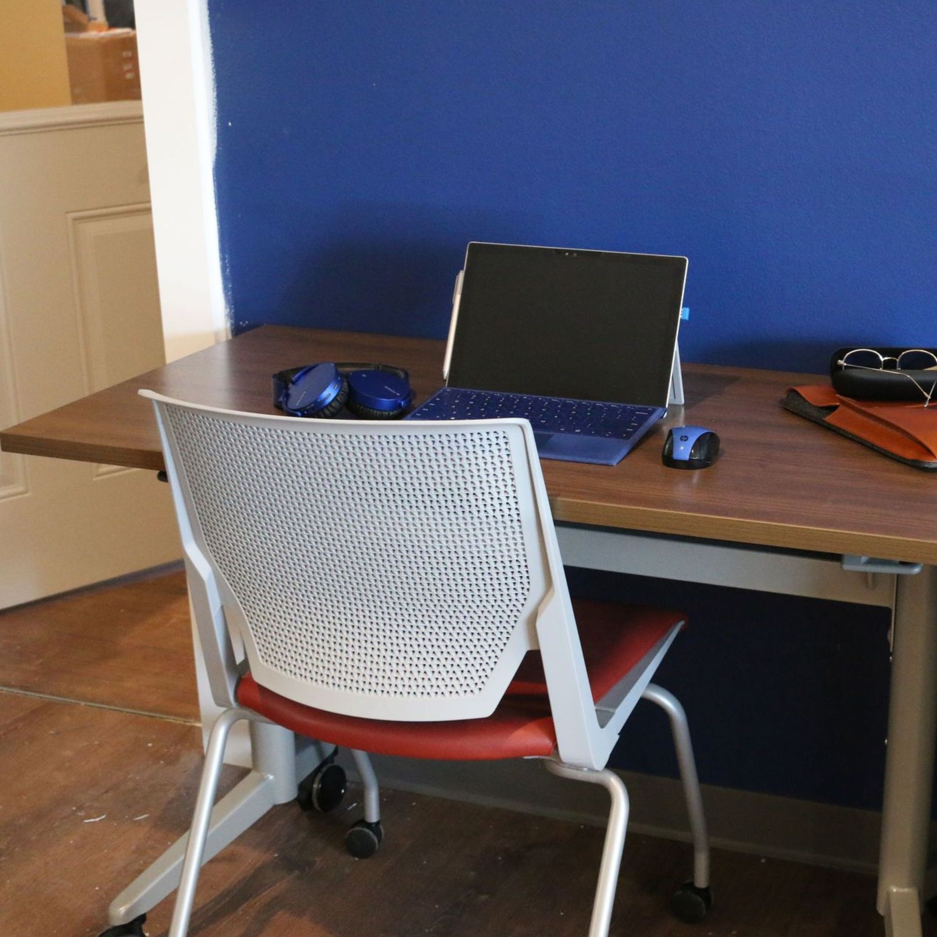 Desk with open laptop, blue wall, white chair, sunglasses, and headphones in a small room.