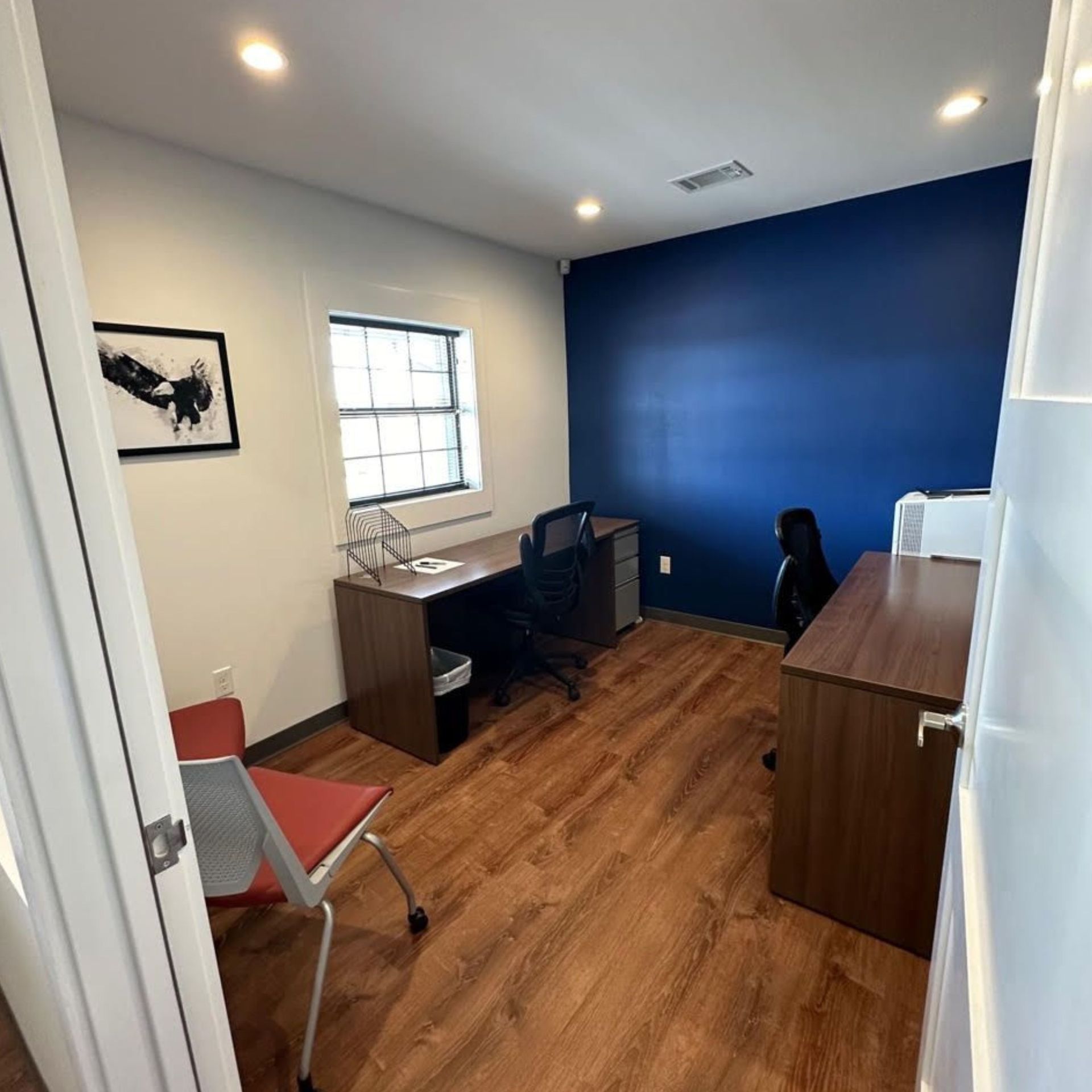 Small office with blue accent wall, wood desk, black chair, and orange folding chair.