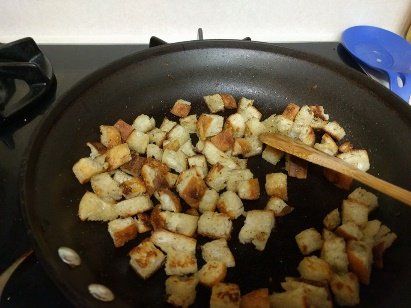 Croutons are being cooked in a pan with a wooden spatula
