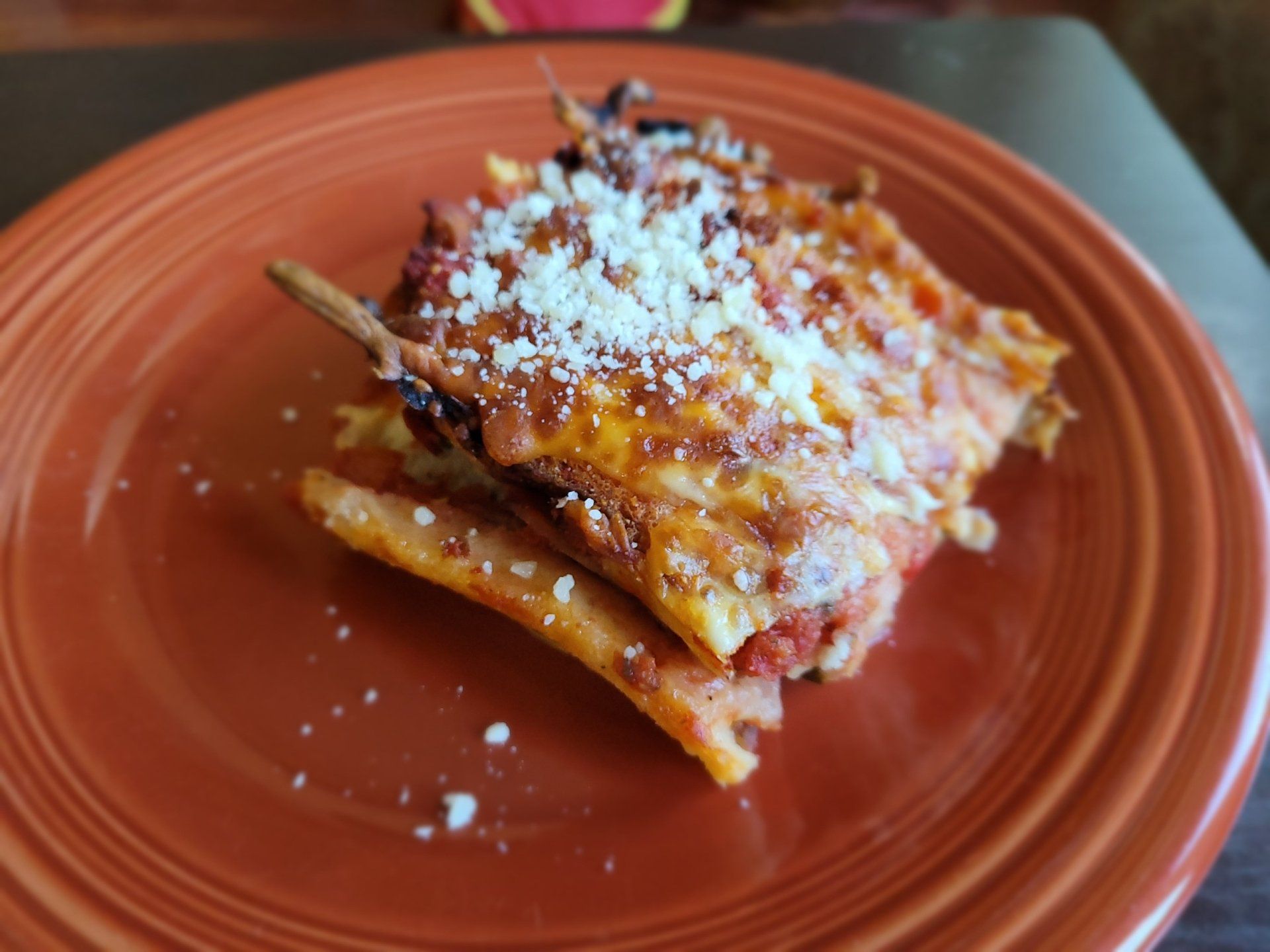 A slice of lasagna on a red plate on a table.