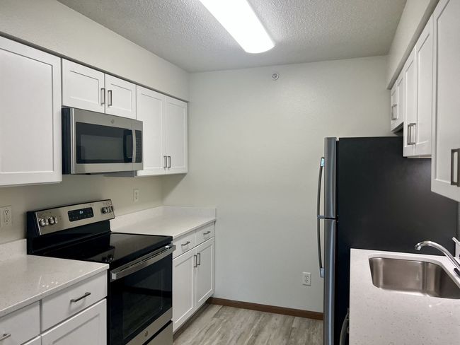 Empty modern kitchen with white cabinets, stainless appliances, and a black refrigerator on the right.