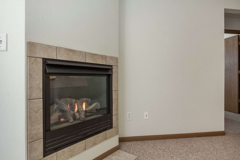 Modern living room with a stone fireplace and beige walls, featuring a lit gas fire.