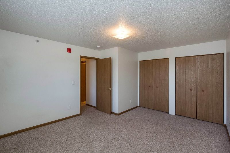 Empty carpeted bedroom with white walls, wooden closet doors, and an open doorway.