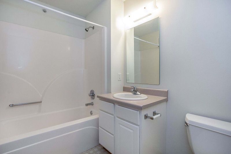 Small white bathroom with bathtub, sink vanity, mirror, and toilet.