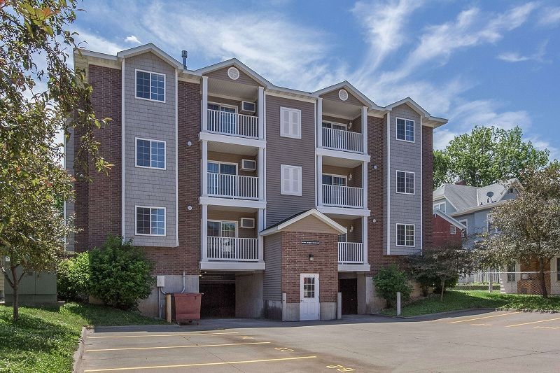 Three-story brick apartment building with balconies and parking lot in front