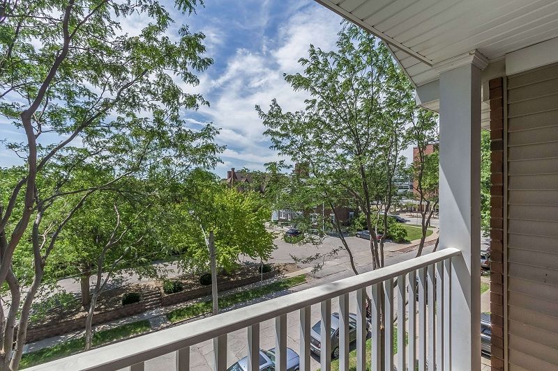 Balcony view of leafy trees, street, and parked cars on a sunny day