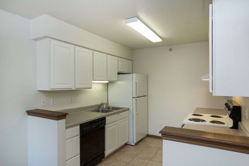 Bright white kitchen with cabinets, stove, refrigerator, and fluorescent ceiling light.