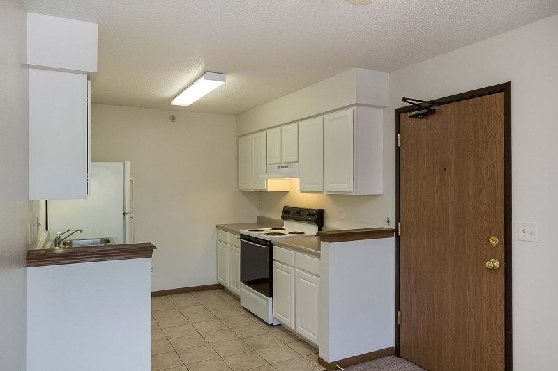 Small kitchen with white cabinets, stove, and brown door on the right.