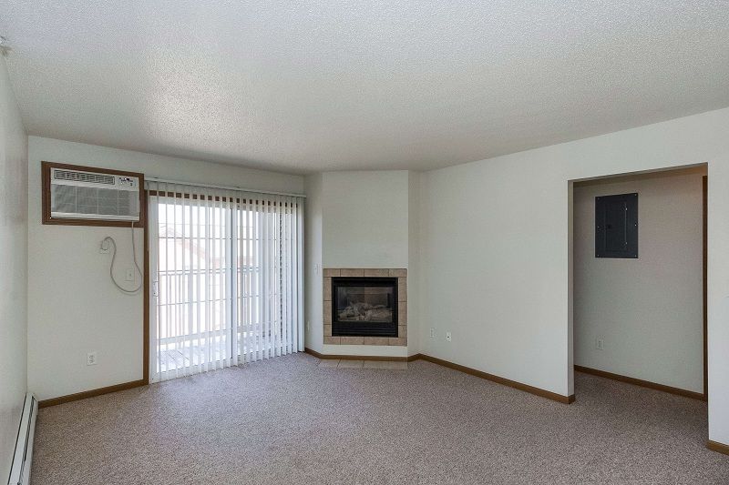 Empty beige living room with carpet, sliding glass doors, fireplace, and a doorway to the right