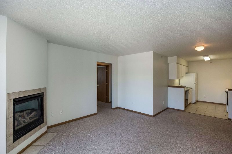 Empty living room with fireplace, carpet, and open view into kitchen and hallway