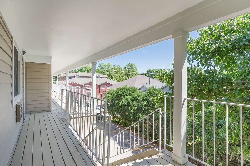 White porch walkway with railings overlooking green trees and neighboring houses under a bright sky