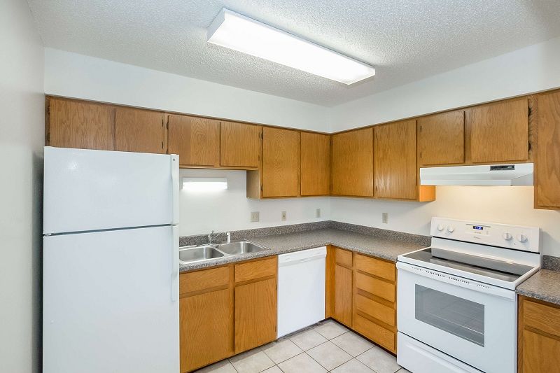 Small kitchen with wood cabinets, white appliances, gray countertops, and tiled floor.