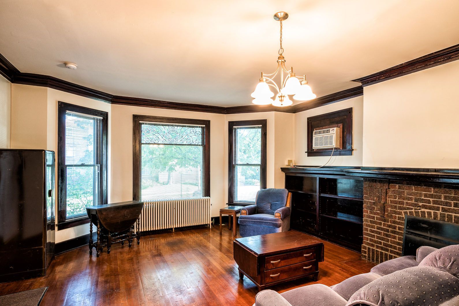 Bright living room with hardwood floors, large windows, fireplace, chandelier, and dark wood furniture