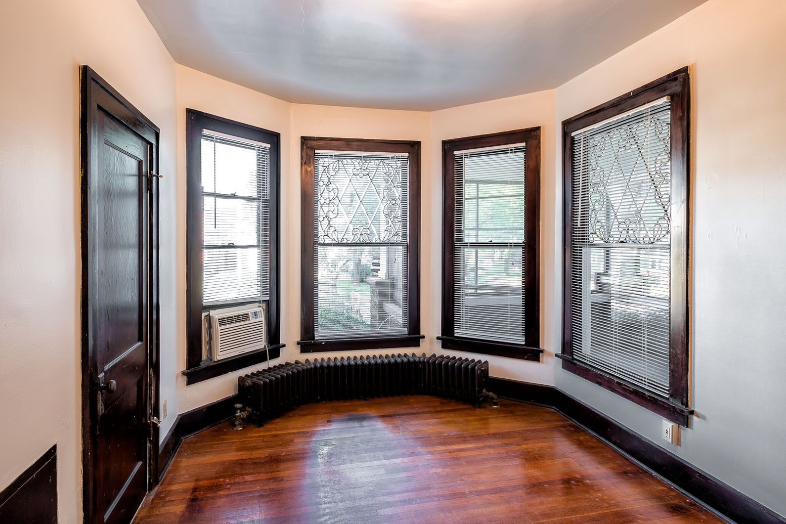 Empty curved bay window room with dark wood trim and hardwood floors.