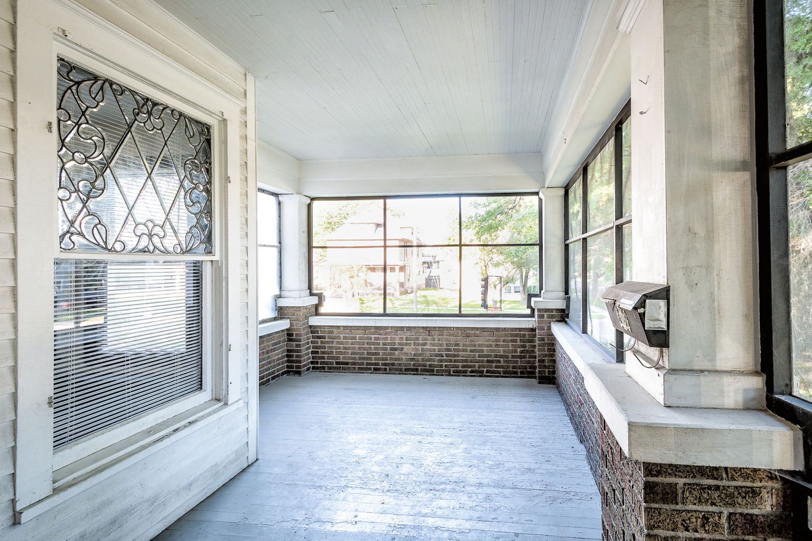 Covered front porch with white columns, screened door, and stone-trimmed windows.
