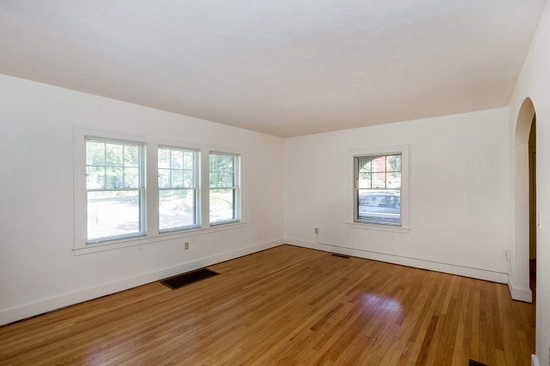 Empty living room with hardwood floors, white walls, and several windows letting in daylight