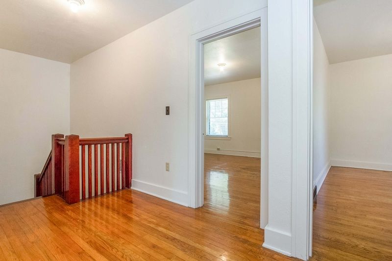 Empty hallway with hardwood floors, white walls, and a red baby gate by a stair railing