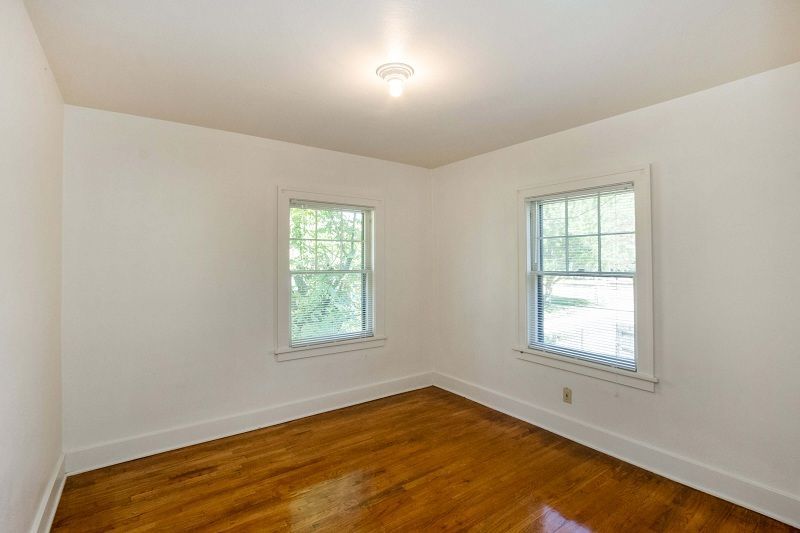 Empty white room with hardwood floor, two windows, and a ceiling light