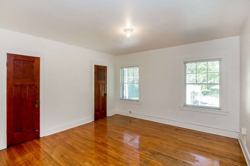Empty room with hardwood floor, white walls, two windows, and a wooden door