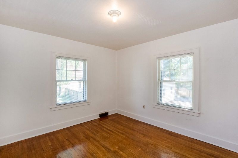 Empty white room with hardwood floors and two windows with blinds