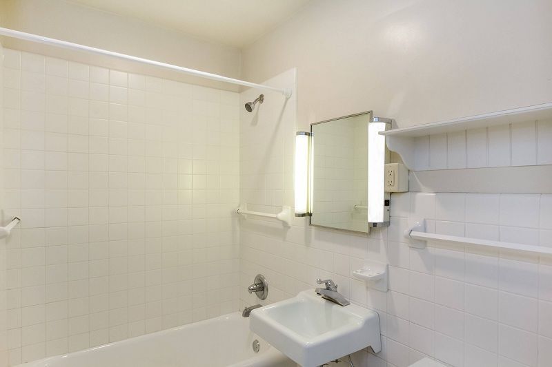 Small white-tiled bathroom with a bathtub, wall mirror, sink, and shower curtain rod.