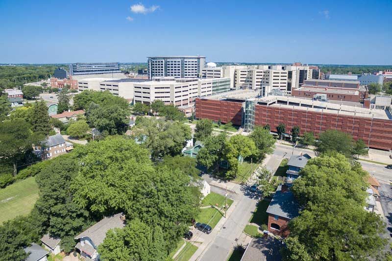 Aerial view of a city with tree-lined streets and large buildings under a clear blue sky