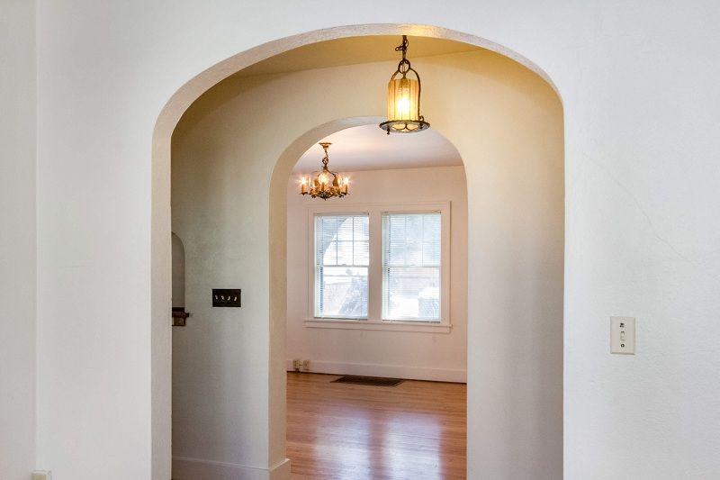 Arched hallway opening to a bright room with hardwood floors and hanging pendant lights