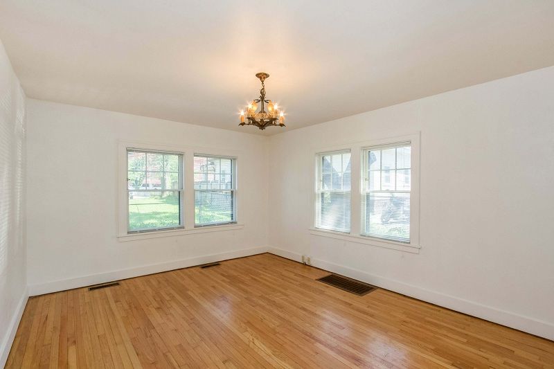Empty white living room with hardwood floors, chandelier, and windows on two walls
