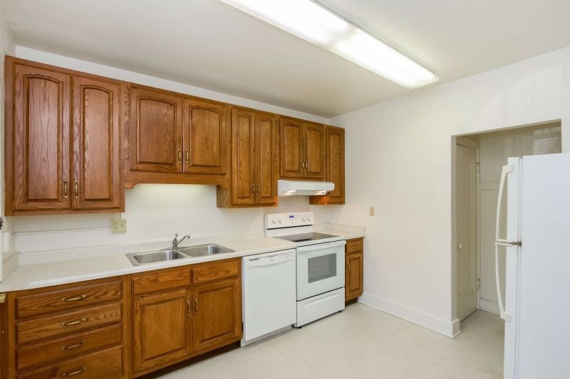 Small kitchen with wood cabinets, white appliances, and a refrigerator in a bright room.
