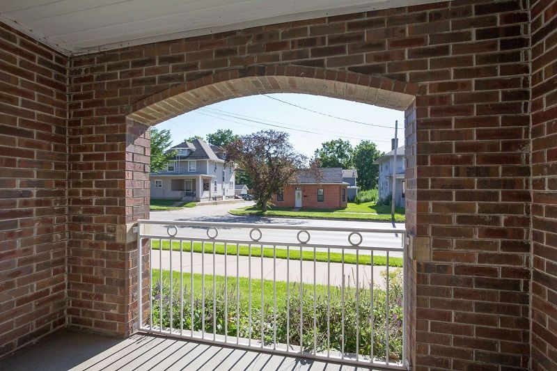 Brick porch arch framing a quiet street and houses beyond a white metal gate
