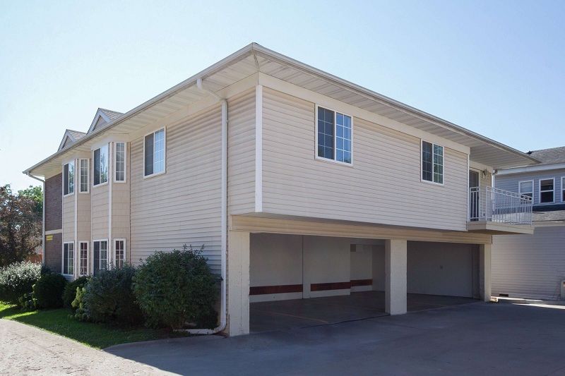 Two-story beige house with white trim and covered carport in a sunny suburban setting
